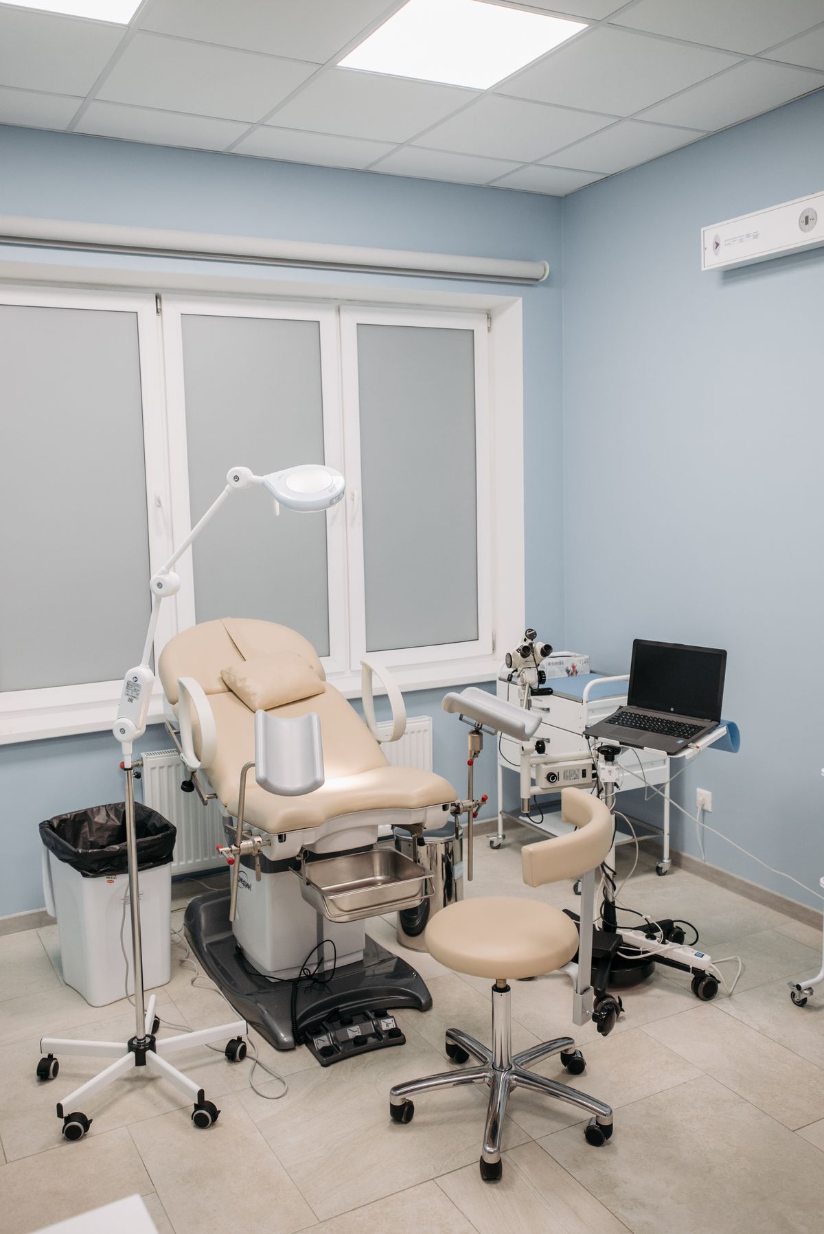 A modern private clinic examination room with treatment chair, procedure light and equipment trolley