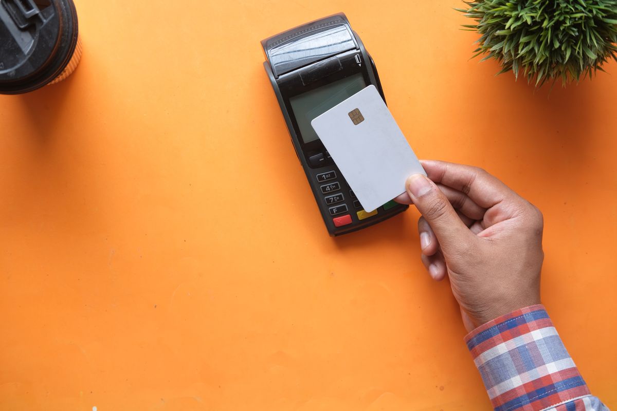 A hand holding a bank card against a contactless card reader