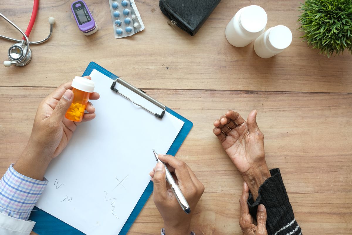Overhead view of a doctor's hands writing a prescription across a desk from a patient