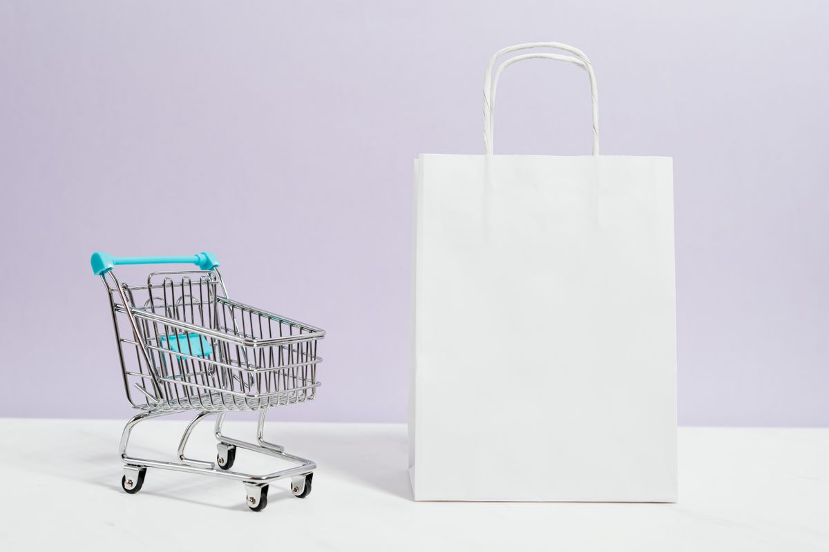 A miniature shopping trolley beside a plain paper shopping bag, representing online retail purchases