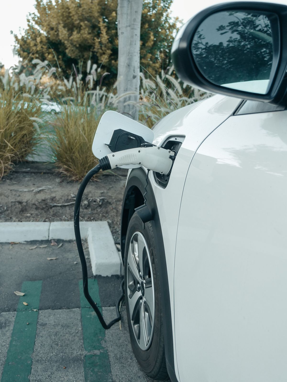 A white electric car plugged into a charging unit at an outdoor parking bay