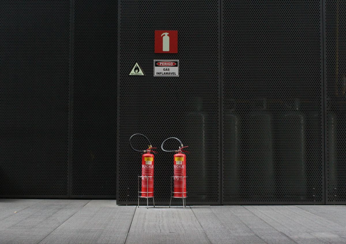 Two red fire extinguishers standing against a dark industrial wall beneath fire and flammable-gas signage