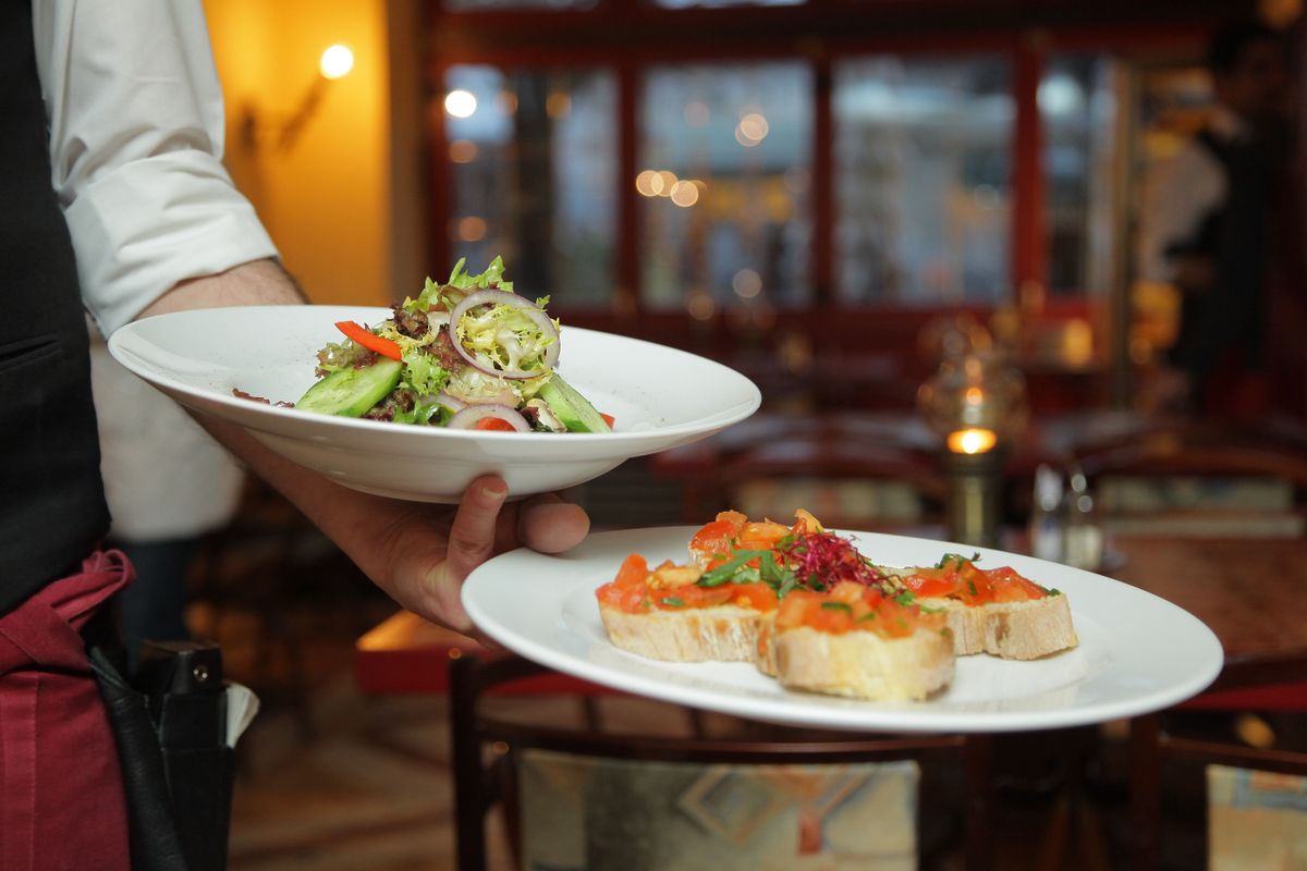 A waiter carrying two plated dishes through a restaurant dining room