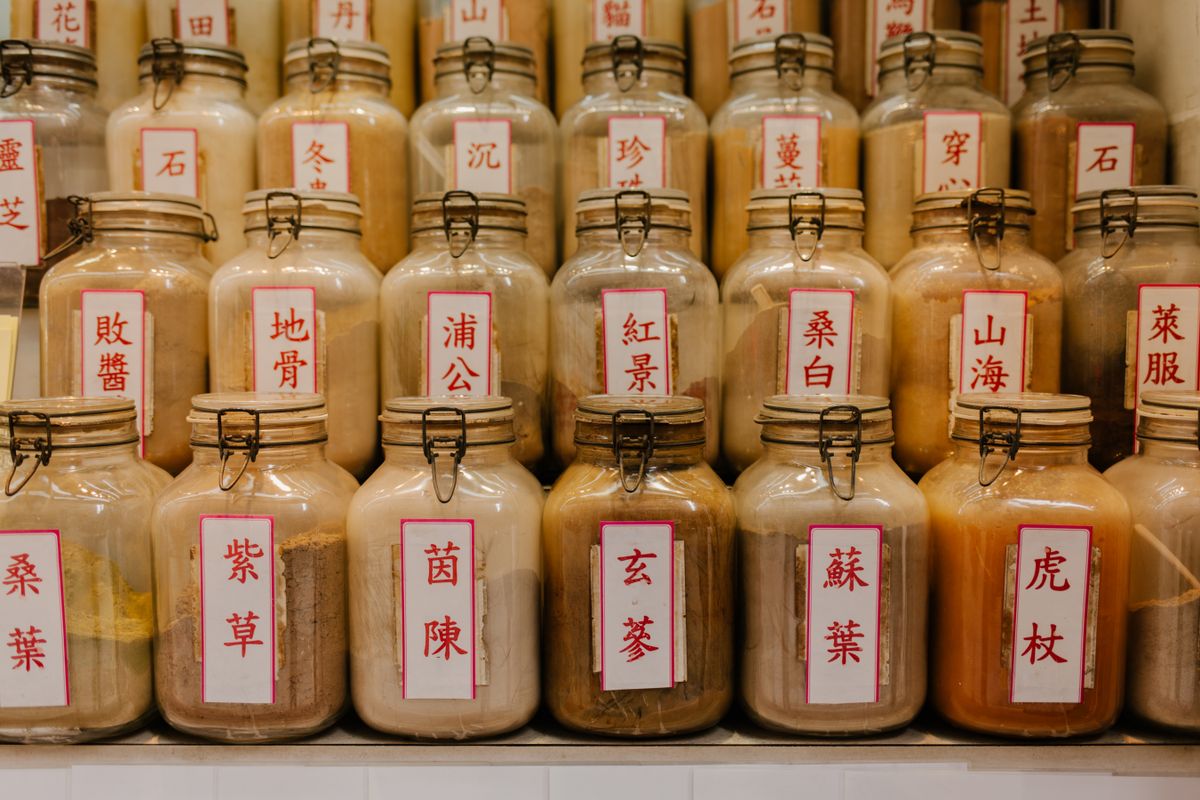 Rows of labelled glass apothecary jars of dried Chinese herbs in a traditional medicine shop